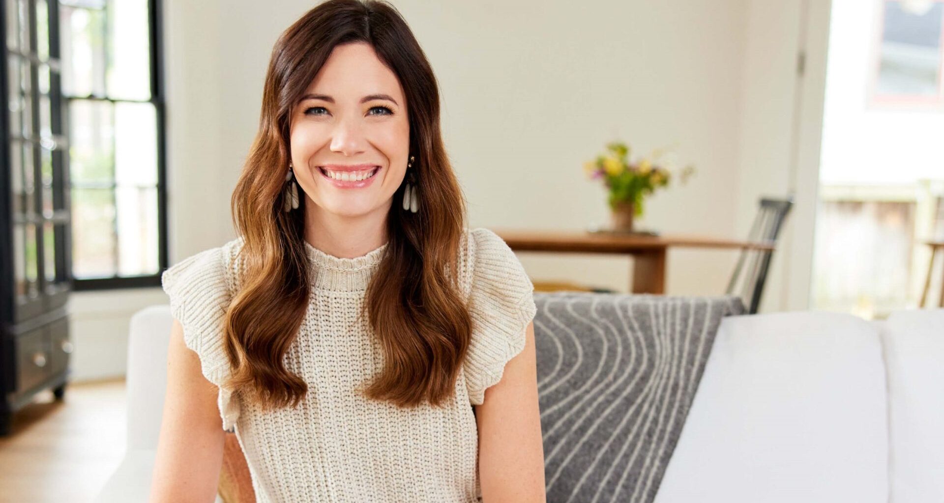 Rachel Cruze smiling at camera while sitting on a couch at a home.