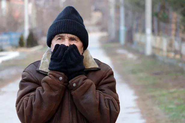 Generic photo of a man stood outside in a hat and a winter coat breathing on his hands to warm them up.  