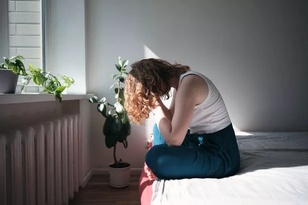 Depressed woman sitting on bed holding head in hands, waking up with depression. Sad anxious female sitting on bed holding head in hands suffering from headache