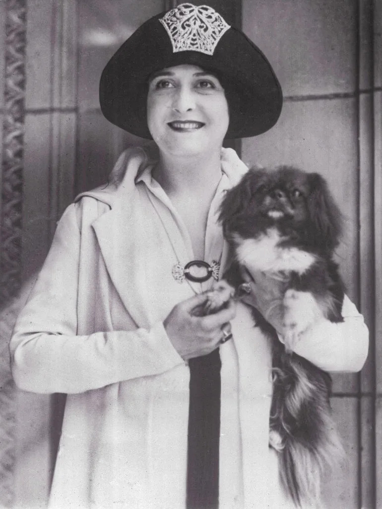 Young in 1920s fashion with embellished hat, holding a small dog