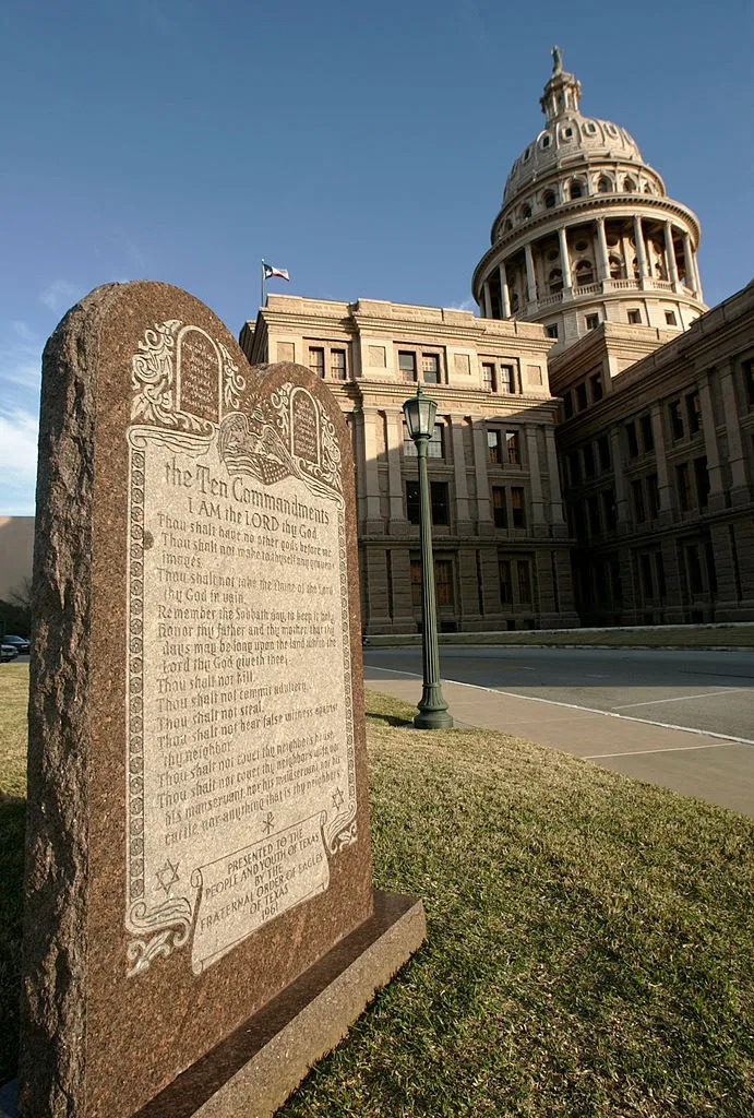 Monument inscribed with the Ten Commandments stands in front of a large government building with a dome