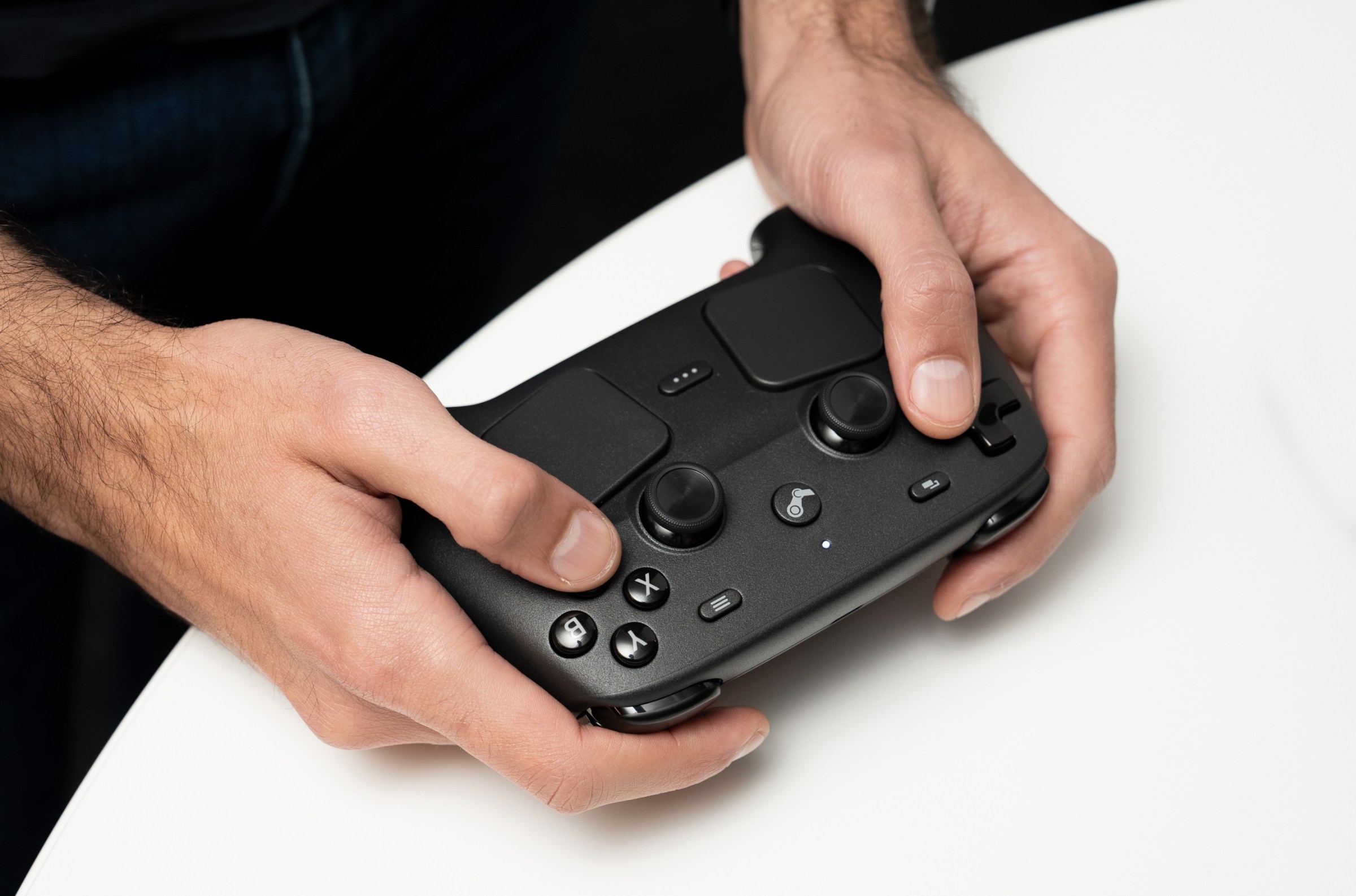 Two hands hold the Steam Controller, thumbs atop the joysticks, with twin touchpads visible underneath them.