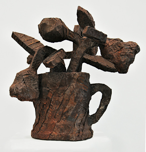 Abstract sculpture resembling a bouquet of flowers in a vase, made from textured, rust-colored material.