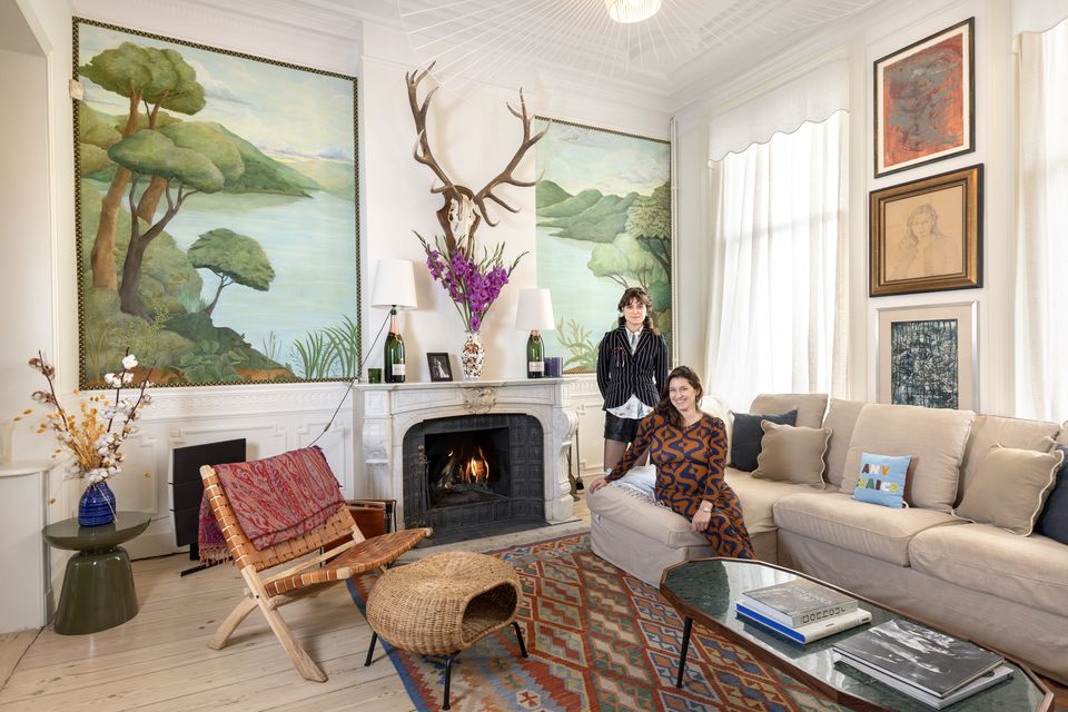 Ashlinn, left, and Alexandra de Schonen in Alexandra’s front reception room, one of three in the four-storey house which dates from the late 1800s. The stars of the decor here are the two panels flanking the fireplace which Ashlinn painted. Alexandra herself made the lamps with the Bollinger bottles. Photo: Tony Gavin