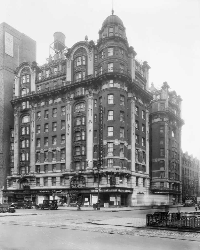 Historic multi-story Hotel Belleclaire with ornate architecture, featuring shops at street level and a cityscape background. Early 20th-century urban scene
