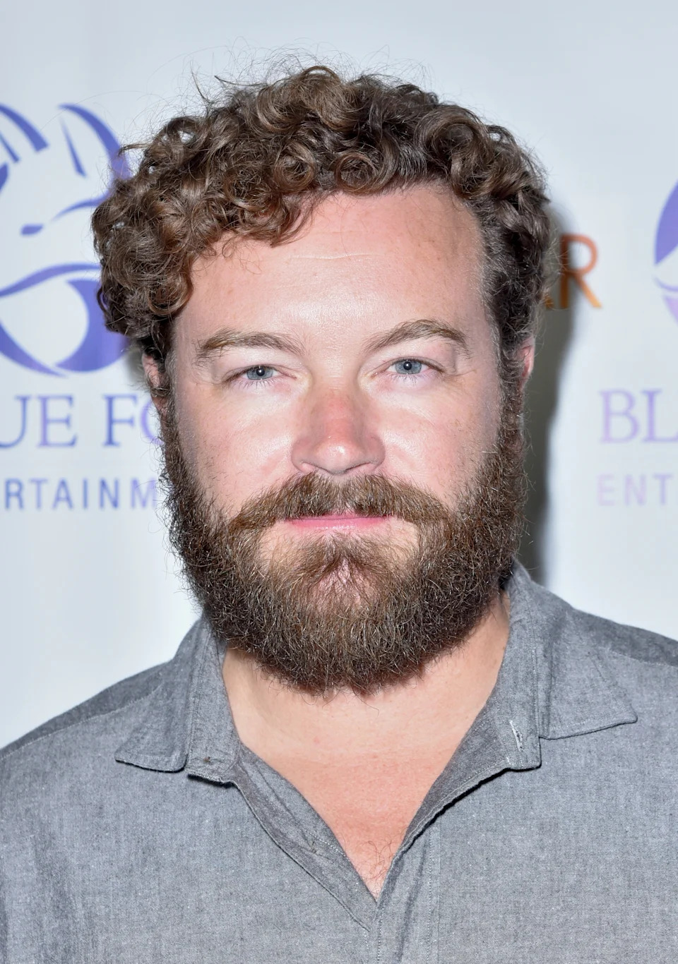 Person with curly hair and beard wearing a casual button-up shirt at a celebrity event