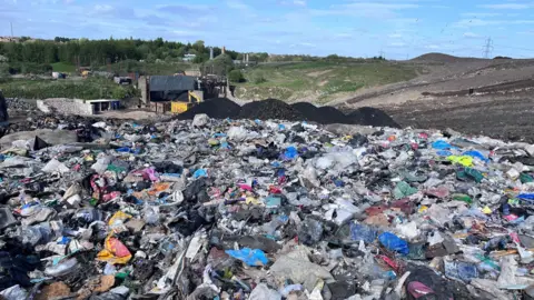 A mountain of rubbish on a landfill site, with countryside in the background.