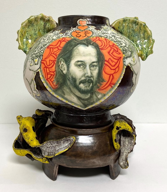 Decorative ceramic teapot with artistic portrait, featuring intricate textures and colorful designs on raised platform.