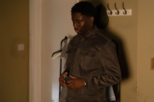 Okie, holding his phone, in EastEnders