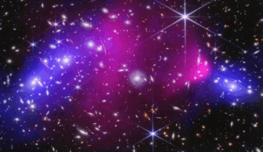 Webb near-infrared data combined with Chandra X-ray data of the Bullet Cluster show many overlapping objects, including foreground stars, galaxies in galaxy clusters, and distorted background galaxies behind the galaxy clusters. The objects are all at various distances set against the black background of space. Most galaxies appear as tiny fuzzy ovals in white, orange, or red. A slightly larger, very bright, light blue spiral galaxy is at center. To its immediate left and right are two large bright pink splotches representing X-rays. The right pink area has a rounded nose facing right, where it is darker pink, and fades to the left as a triangular shape. This is referred to as the Bullet. To the far left and far right, next to the pink regions, are two blue regions representing dark matter mass. The left blue region is a large, long oval at an angle. The blue region at right is a far smaller oval.