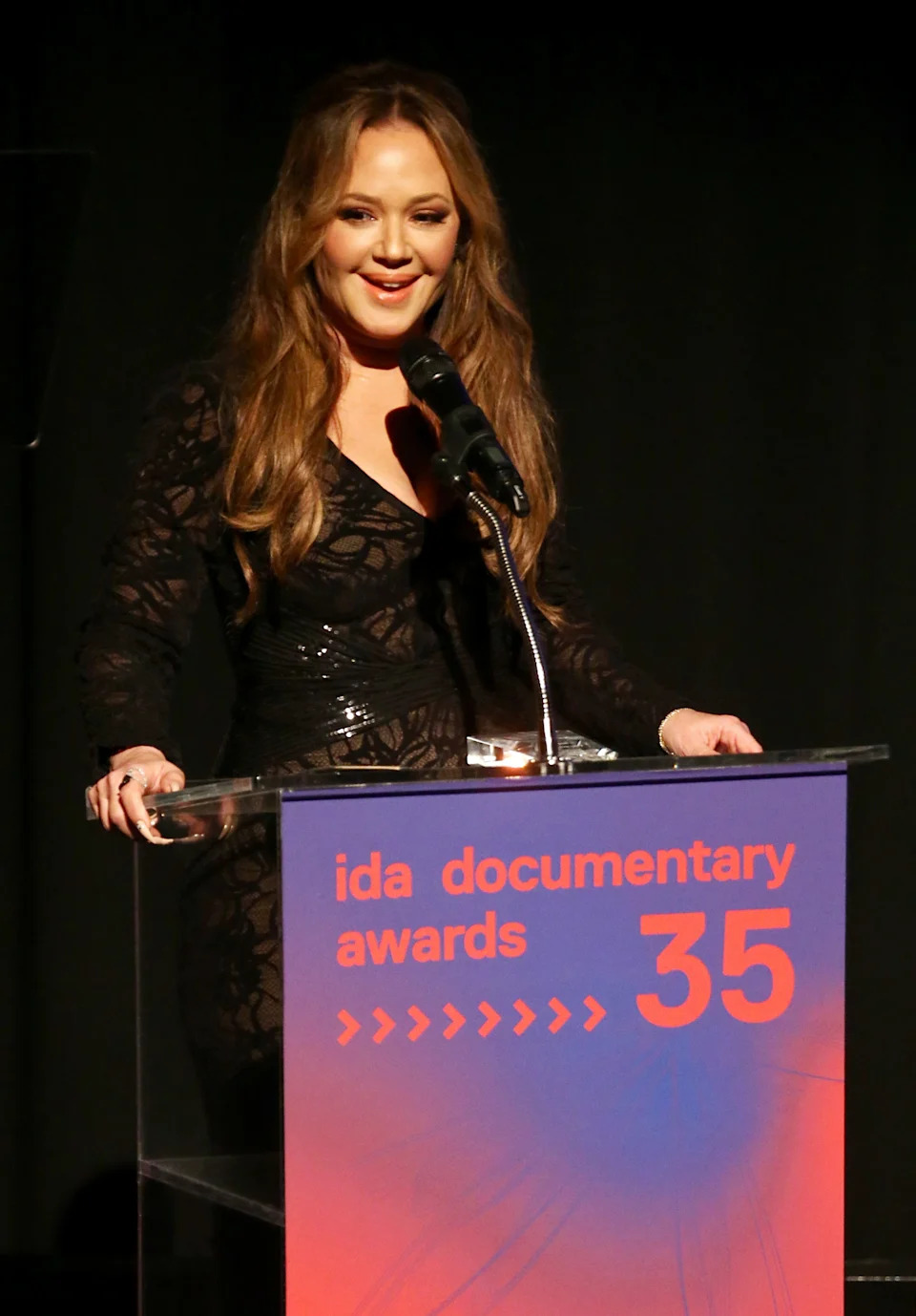 Celebrity in a sheer, embroidered dress speaks at a podium during the IDA Documentary Awards