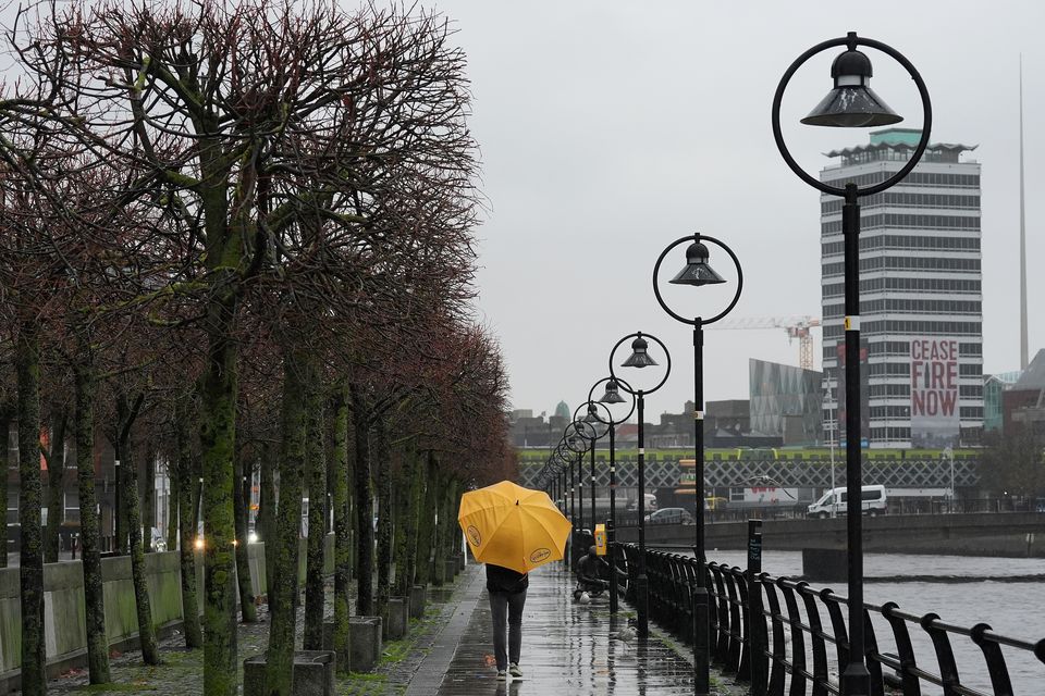 A person holding an umbrella walks along the quays on a wet and windy afternoon in Dublin. Photo: Brian Lawless/PA