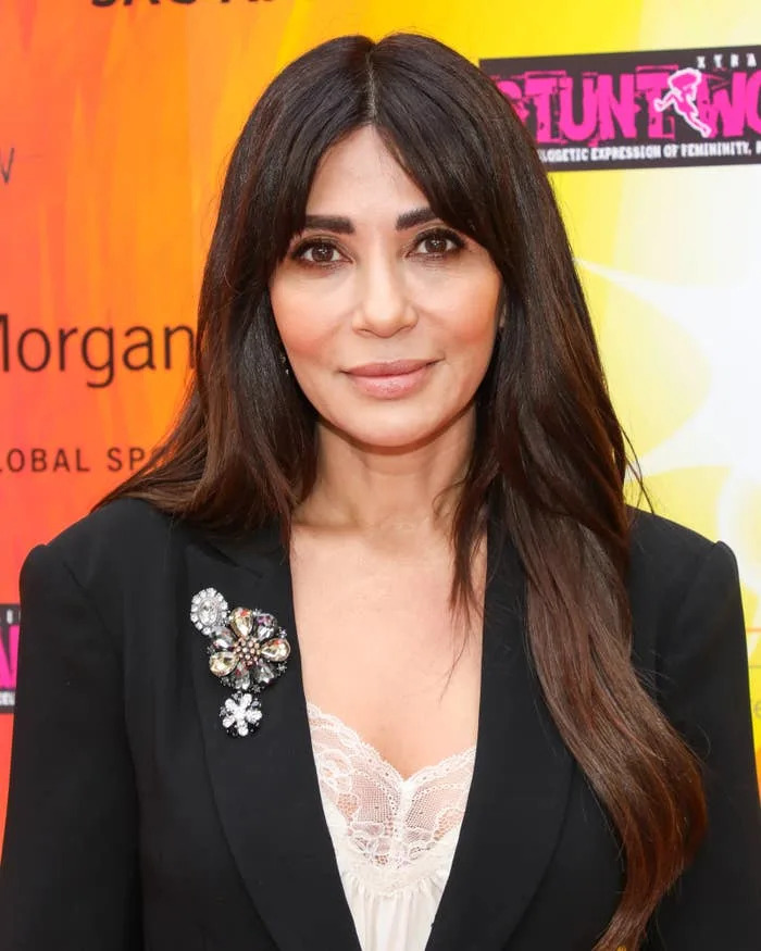 Person in elegant blazer with decorative brooch over lace top, on a colorful backdrop at a celebrity event