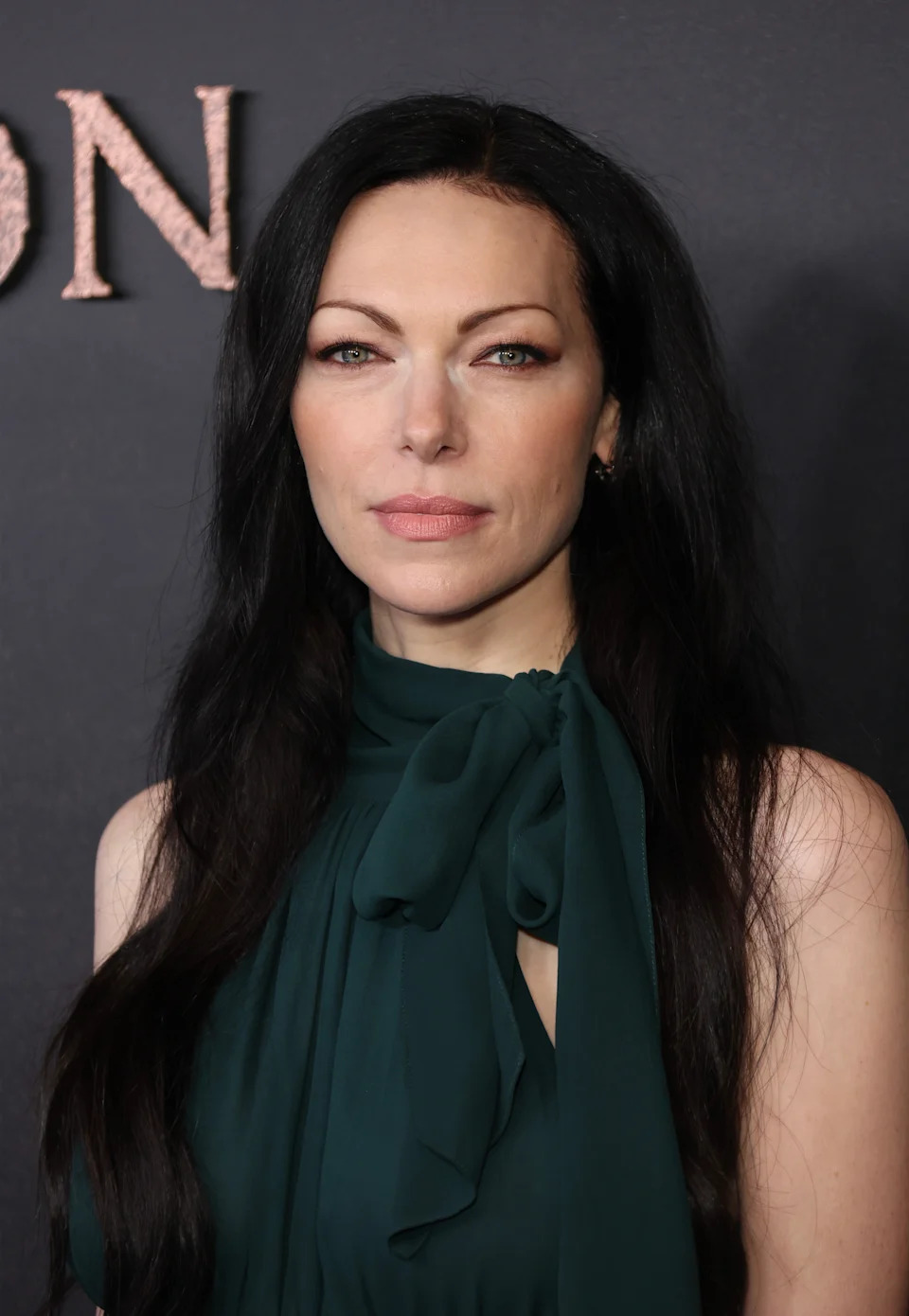 A person with long dark hair in a sleeveless, high-neck gown poses for a photo at a celebrity event
