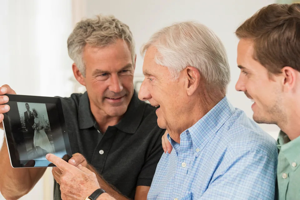 Three men looking at a tablet displaying an old wedding photo, smiling and engaged in conversation