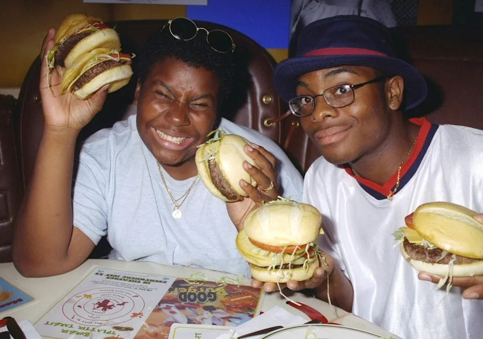 Two people smiling and holding large burgers at a restaurant table, enjoying their meal