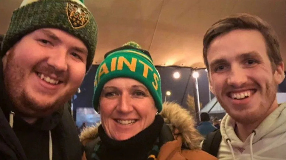 Three people - a smiling young man in green woollen hat on the left; a middle-aged woman in the centre in a green and yellow hat that says "Saints"; a young man on the right smiles with short brown hair.