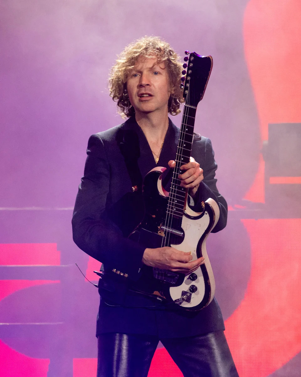 Musician performing on stage, holding a custom electric guitar, wearing a tailored suit jacket and leather pants