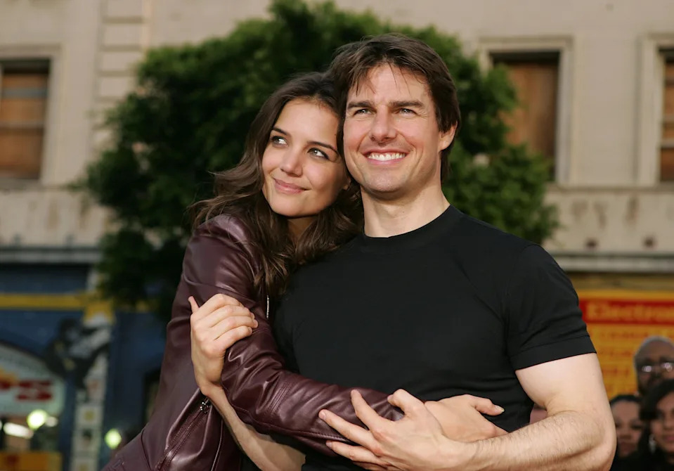 A woman in a leather jacket embraces a man in a t-shirt, both smiling outdoors at an event