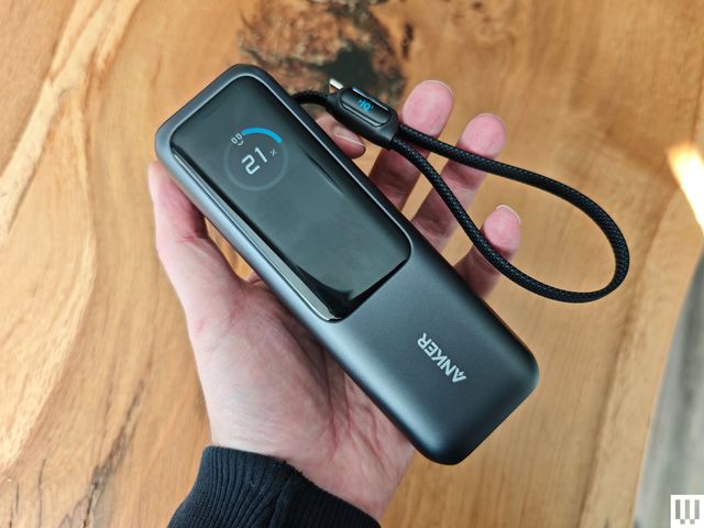 A hand holding an Anker Laptop Power Bank, a black rectangular portable charger with long digital screen.