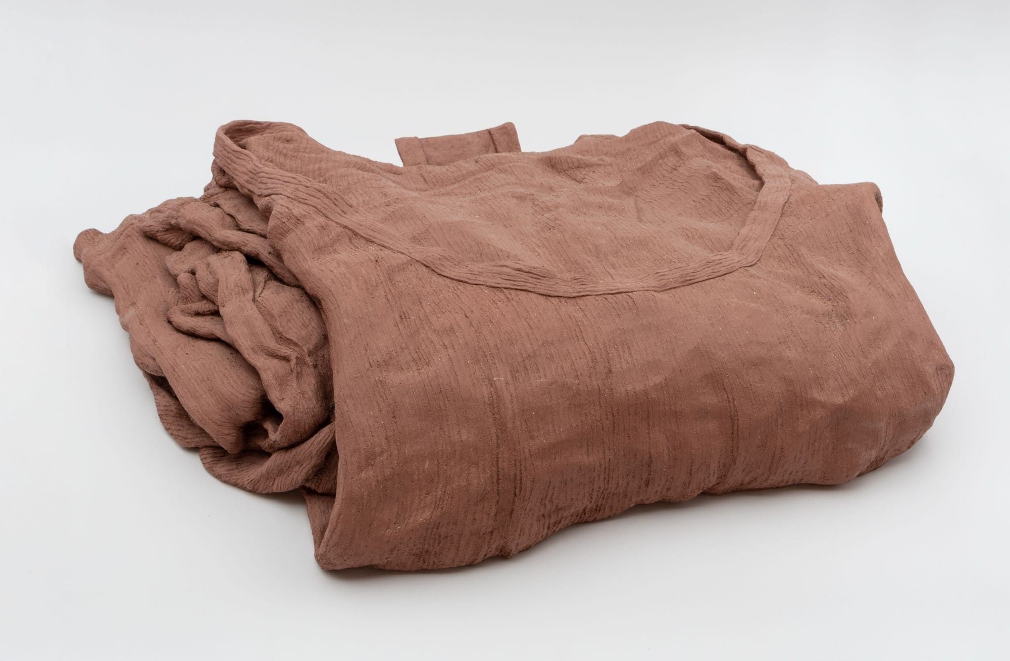a ceramic sculpture by Léonore Chastagner that looks like a folded t-shirt made of red clay