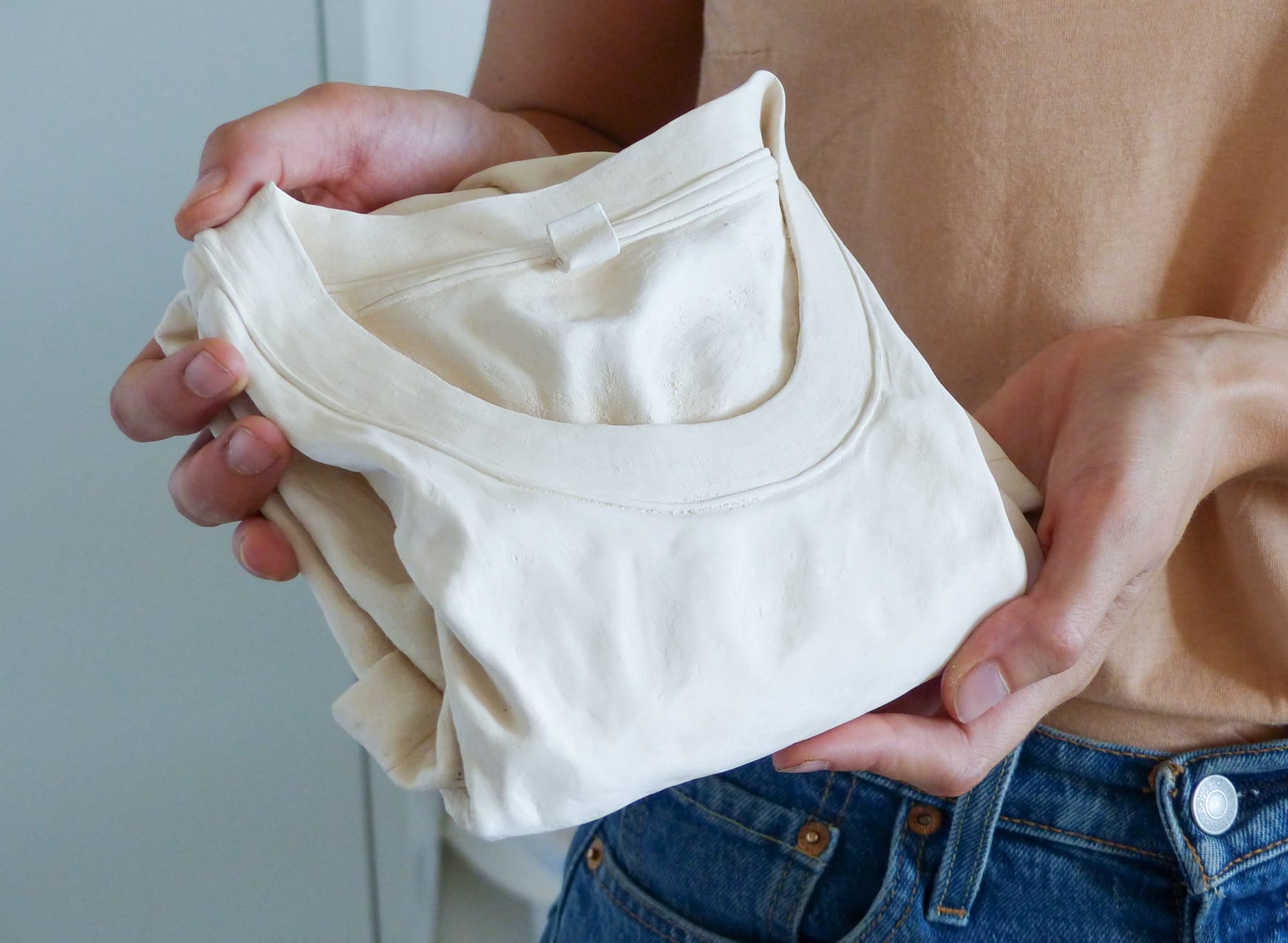 a clay sculpture by Léonore Chastagner of a white, folded t-shirt, held in the artist's hands