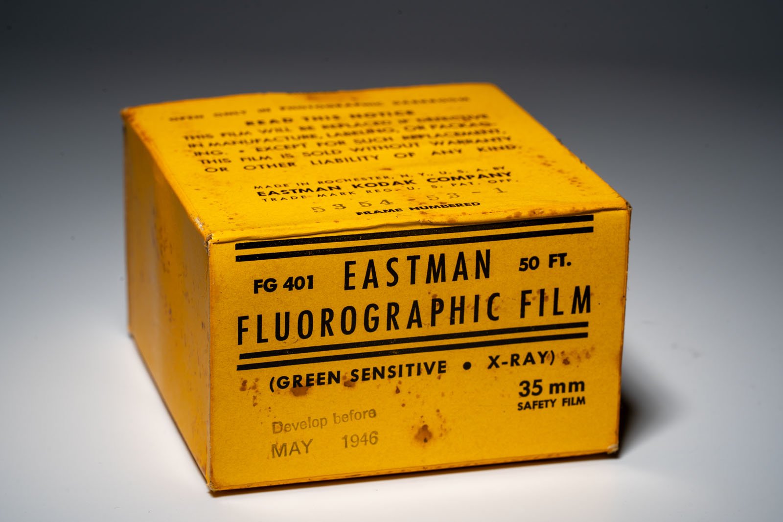 A yellow box labeled "Eastman Fluorographic Film" for 35mm safety film, 50 feet long, green-sensitive and for X-ray use, with a "Develop before May 1946" notice and signs of age and rust spots.