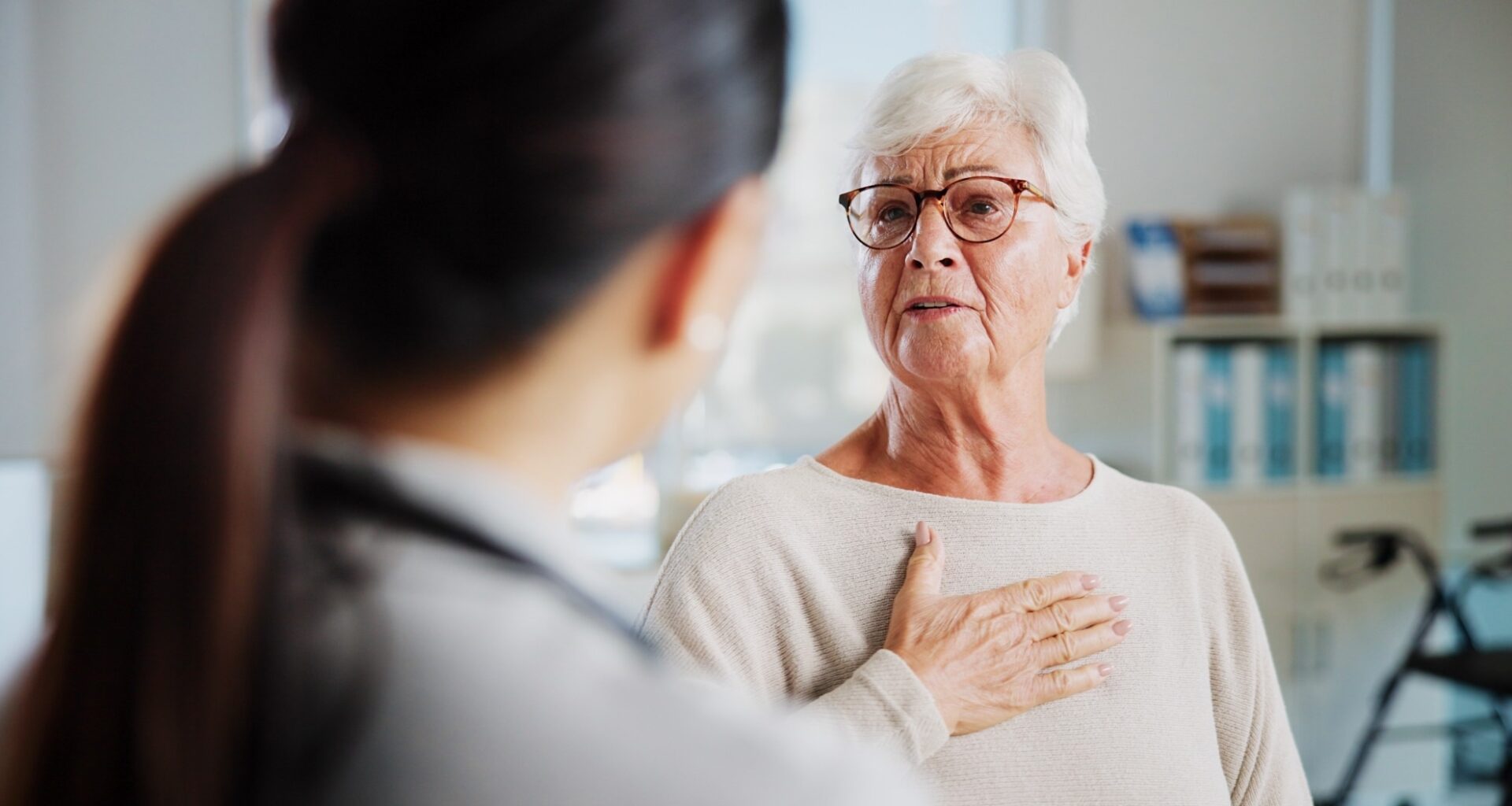 Elderly lady holding chest in pain whilst talking to a healthcare worker