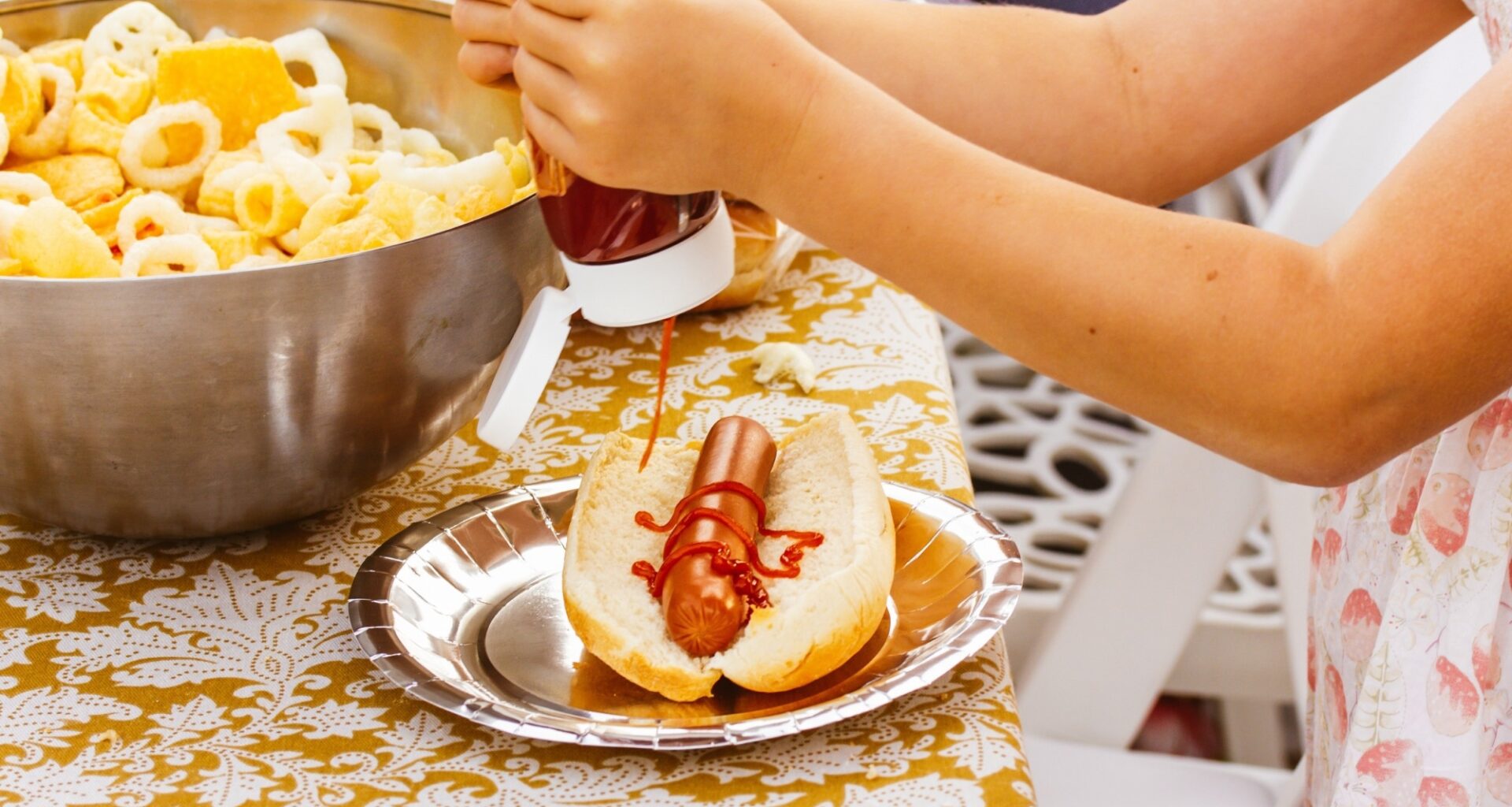 A little girl squeezing ketchup on a hotdog