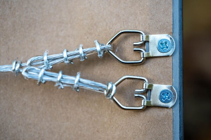 Close-up of two metal picture hanging hooks screwed into the back of a wooden frame, with twisted wire securely attached to each hook.