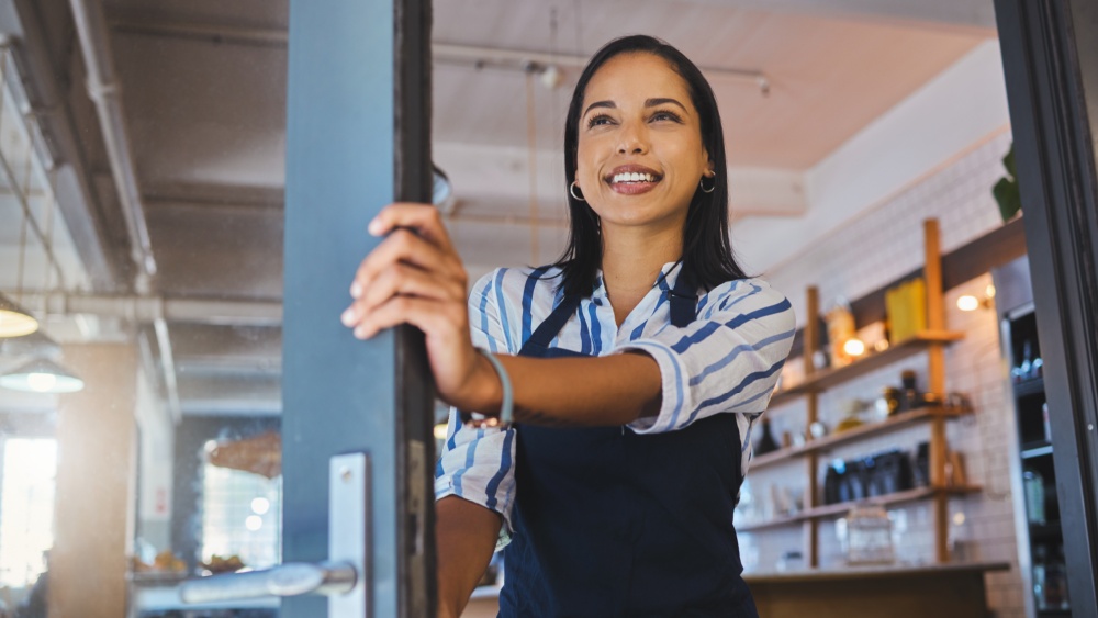 women in apron opening a door to a business