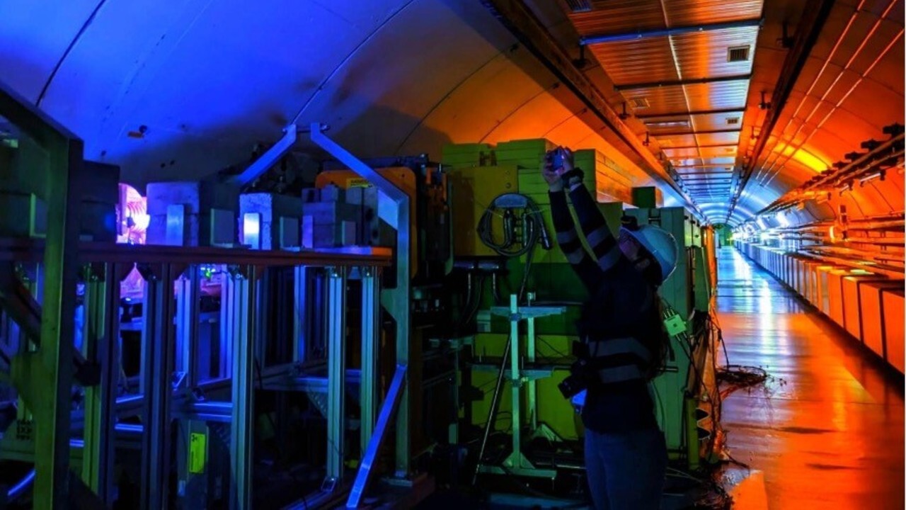 A dimly lit hallway with orange lights shows a series of laboratory experiments lit up in blue and green lights