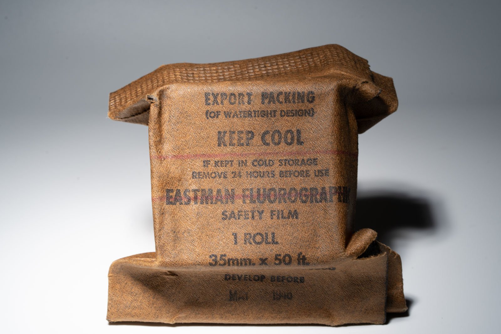 A brown, textured package labeled "EASTMAN FLUOROGRAPH SAFETY FILM, 1 ROLL, 35mm x 50 ft." The label includes instructions to keep cool and a "Develop Before" date of May 1940.