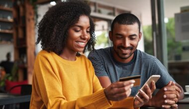 A young women holding a mobile phone and a credit card while smiling with a young man beside her.