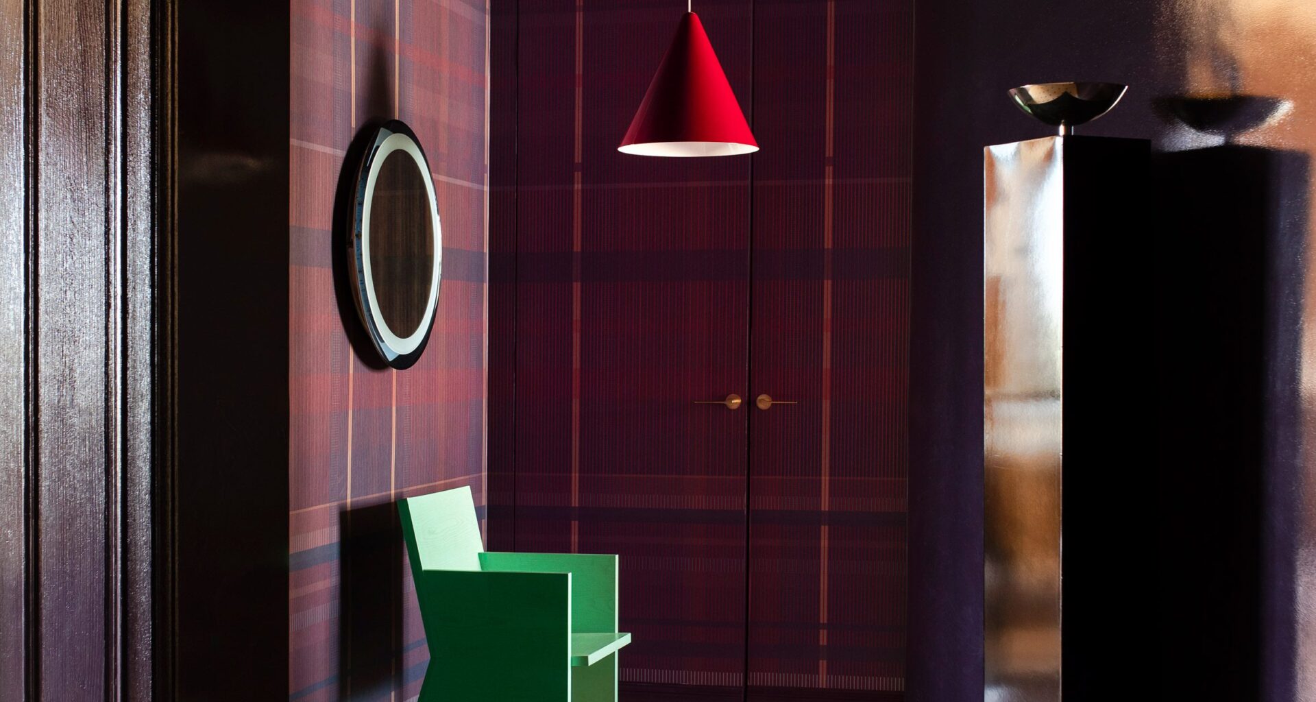 Photograph of the dramatic entrance hall, which has tartan wallcoverings in a deep purple. There is a patterned marble floor, and a green sculptural chair, spotlighted by a red-hanging pendant light.