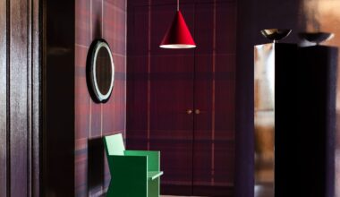 Photograph of the dramatic entrance hall, which has tartan wallcoverings in a deep purple. There is a patterned marble floor, and a green sculptural chair, spotlighted by a red-hanging pendant light.