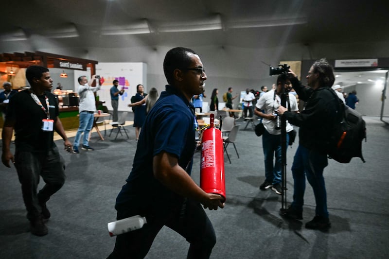 A worker runs carrying a fire extinguisher toward a pavilion after a fire broke out during the COP30 UN Climate Change Conference in Belem. Photograph: Pablo Poriuncula/AFP
