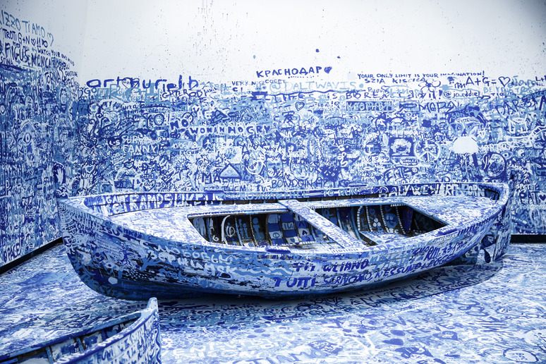 Blue boat covered in white graffiti surrounded by a similarly painted room, creating a monochromatic art installation.
