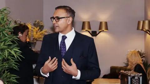 Jas Bains Jas Bains in a smart suit in a swanky bar restaurant talking to people who are out of shot