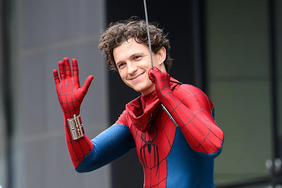 Tom Holland as Spider-Man costume waving, smiling outdoors