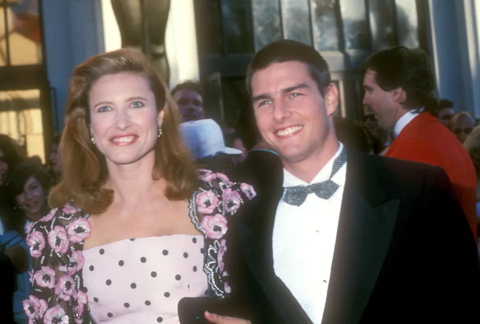 Two celebrities on a red carpet. The woman wears a floral dress with a polka-dot pattern. The man is in a tuxedo with a bow tie