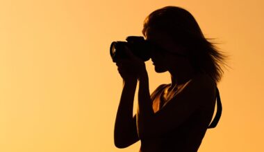 Silhouette of a person holding a camera and taking a photo against a bright orange-yellow background, likely at sunset or sunrise.
