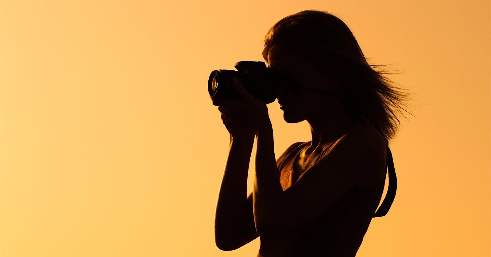 Silhouette of a person holding a camera and taking a photo against a bright orange-yellow background, likely at sunset or sunrise.