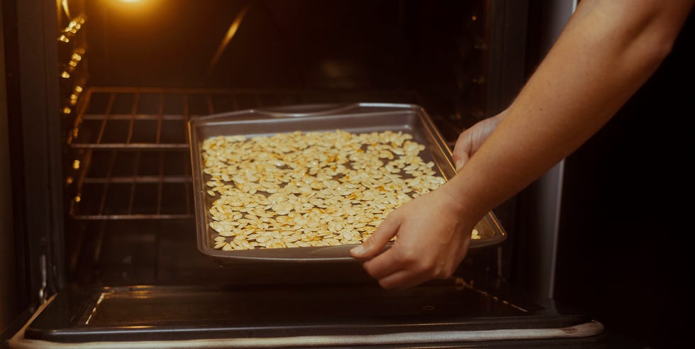 Close up of a baking sheet full of pumpkin seeds being placed in a oven close up of a baking sheet full of pumpkin seeds being placed in a oven