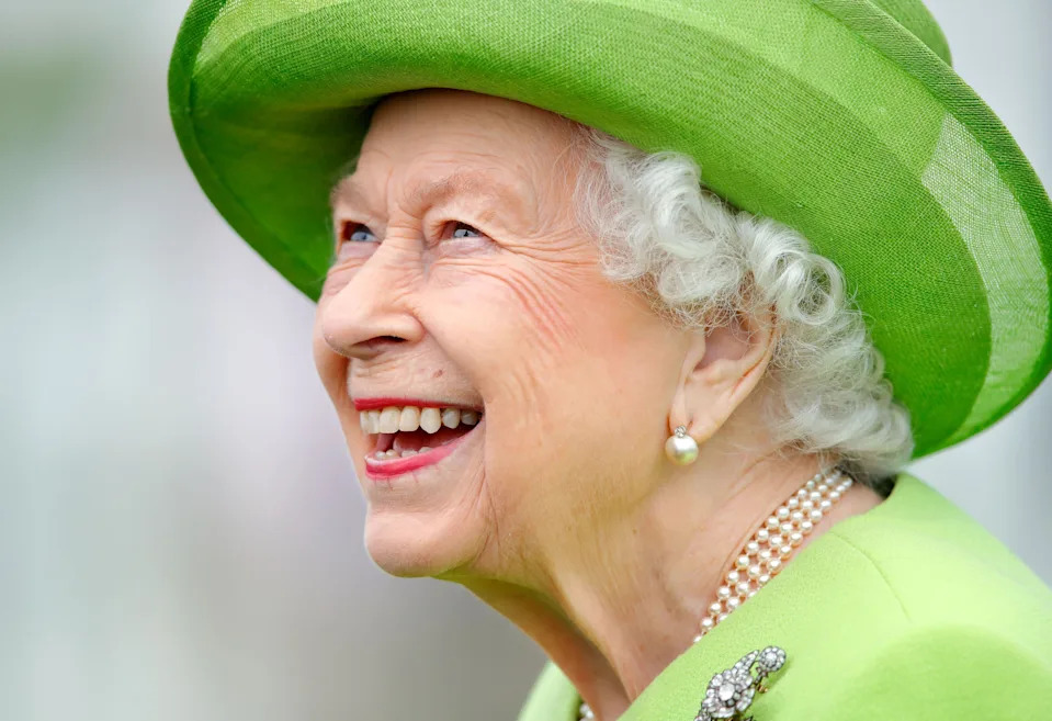 Queen Elizabeth gives a big smile while wearing a bright green coat with a matching hat.