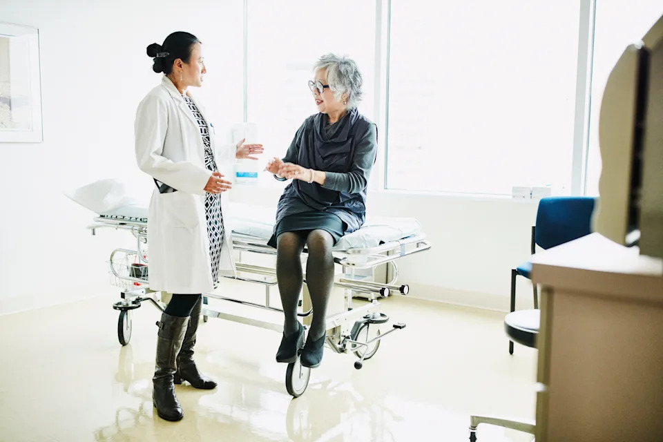 Doctor speaking with an older patient seated on a medical exam table in a well-lit room