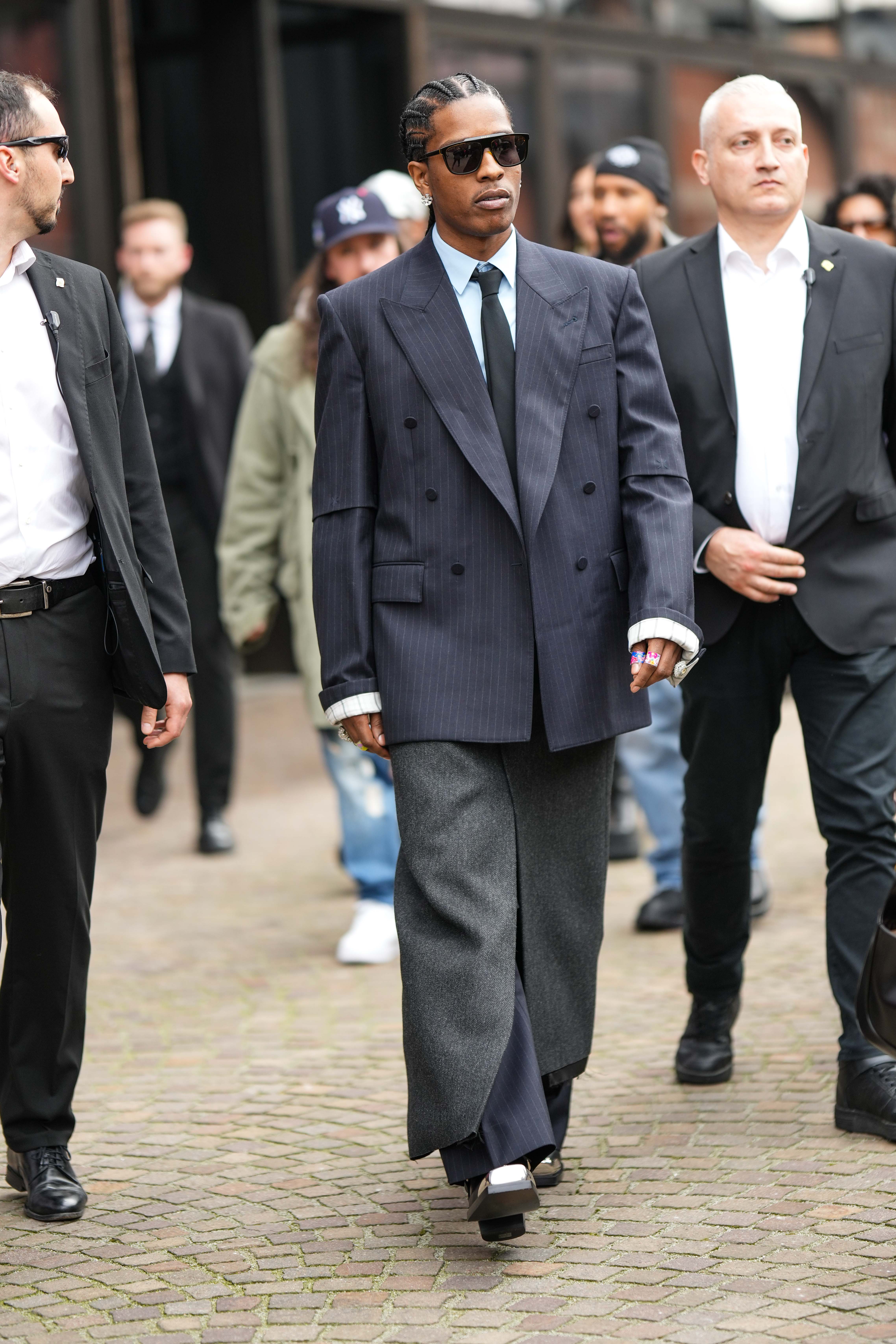 milan, italy february 24: asap rocky wears black sunglasses, a white shirt, a black tie, a black striped print pattern oversized blazer jacket, a gray slit / split long skirt, matching gray suit pants, white shiny leather block heels ankle boots, rings , outside gucci, during the milan fashion week womenswear fall/winter 2023/2024 on february 24, 2023 in milan, italy. (photo by edward berthelot/getty images)