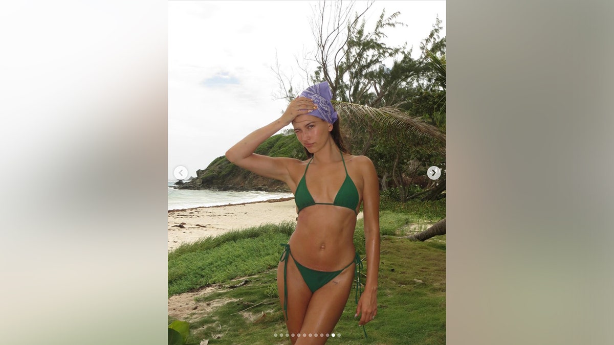 Hailey Bieber in a green bikini and purple bandanna while on the beach.
