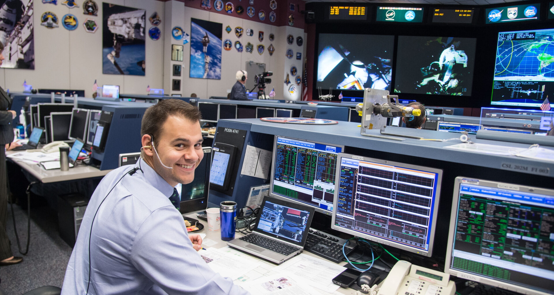 A man wearing a headset sits at a computer console in the Mission Control Center at Johnson Space Center.