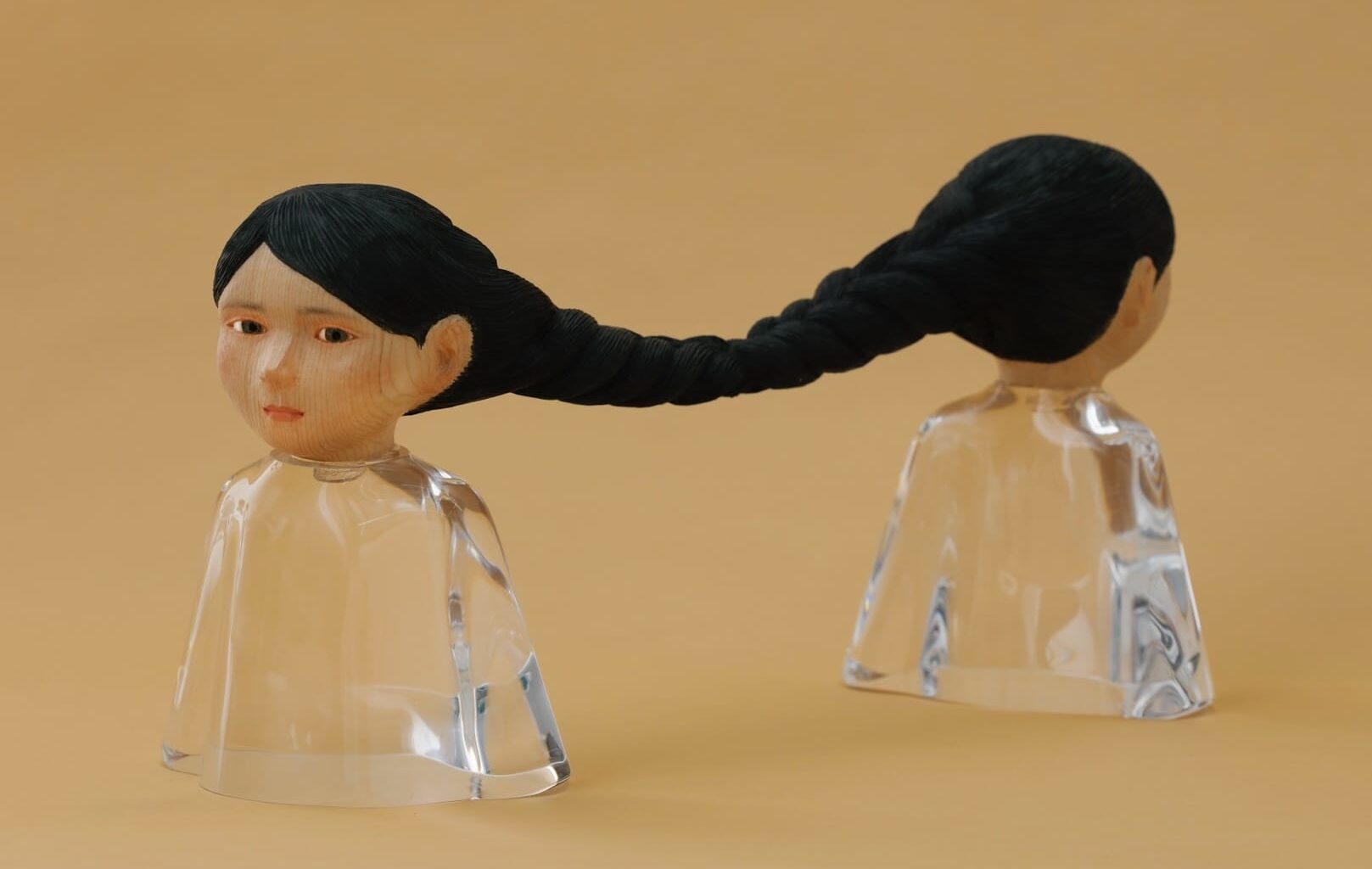 a small sculpture by Ayako Kita made of cypress and acrylic resin, depicting two female figures standing back-to-back with long black hair that is braided together